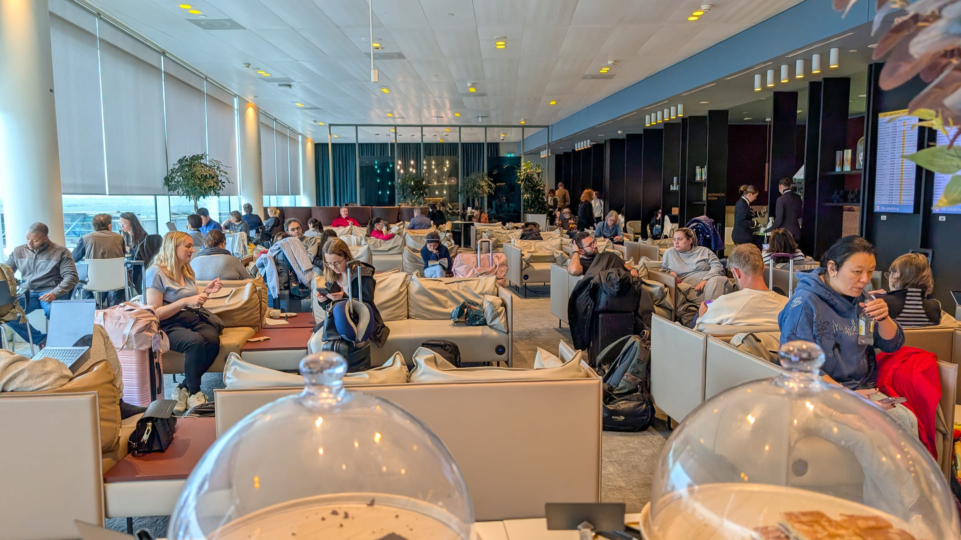 Überfüllter Hauptbereich der Aspire Lounge 41 am Flughafen Amsterdam Schiphol mit vielen Reisenden auf beigen Sofas und eingeschränkter Privatsphäre.